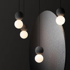 A pair of dark stone pendants with opal glass globes from this Clérachic collection hangs beside a large grey sculptural form.