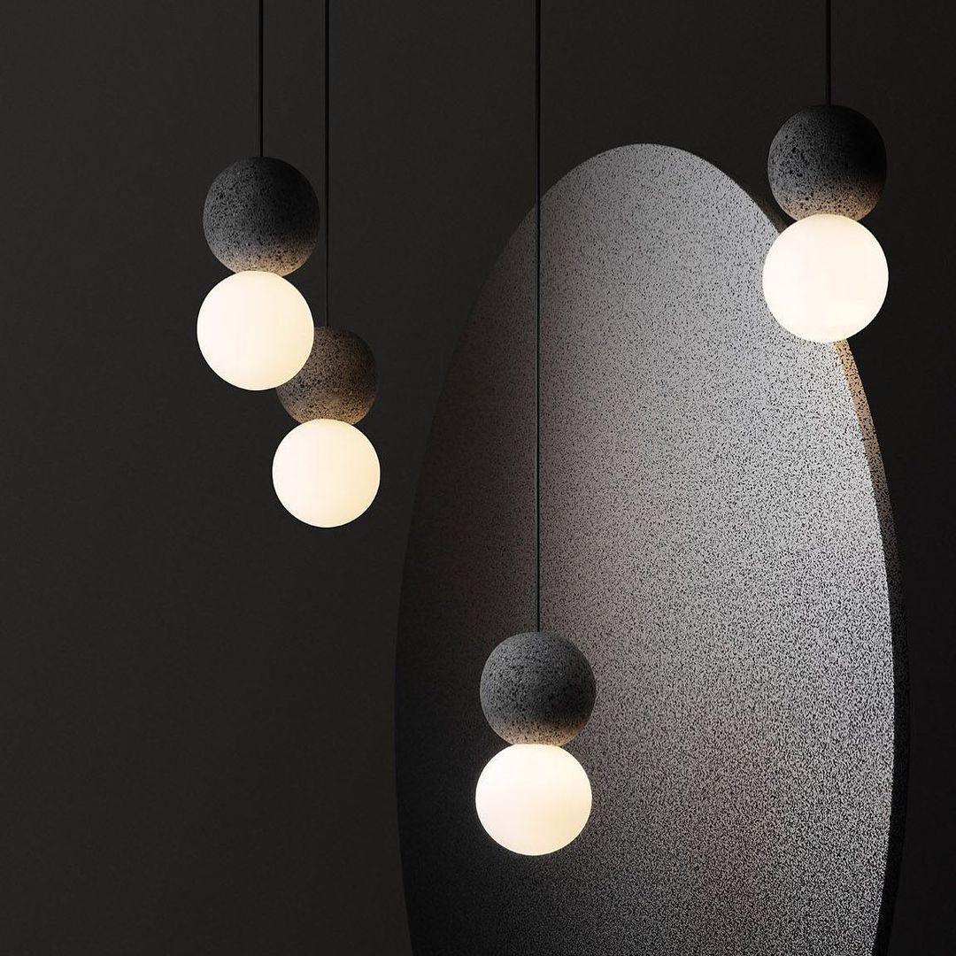 A pair of dark stone pendants with opal glass globes from this Clérachic collection hangs beside a large grey sculptural form.