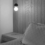 This Clérachic pendant, a small dark sphere and glass globe, hangs beside a grey wood-panelled headboard.