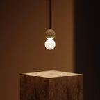 This Clérachic pendant, a dark sphere over an opal glass globe, hangs above a wooden plinth in warm, low light.