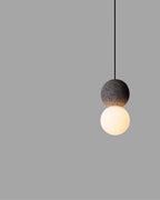 This Clérachic pendant, a dark sphere above a warm-lit glass globe, floats against a plain grey backdrop.