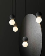 Multiple dark pendants from this Clérachic collection hang beside a large oval sculptural form on a near-black backdrop.