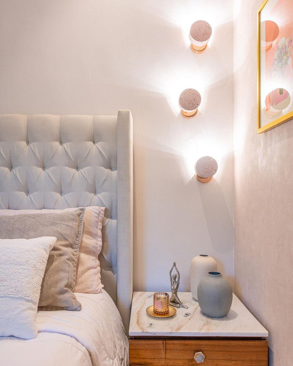 Dusty-pink Clérachic pendants of different sizes hang beside an upholstered headboard in a soft pink bedroom.
