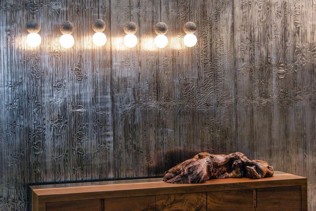 A row of pale glass pendants from this Clérachic collection lights a wood-panelled wall above a low wooden sideboard.