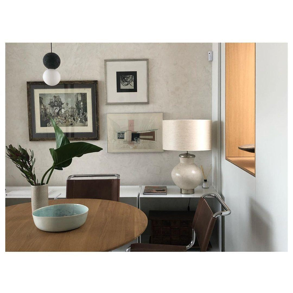A single dark sphere pendant from this Clérachic collection hangs low in a room with framed art and a table lamp.
