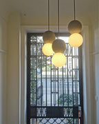 A cluster of stone-textured pendants from this Clérachic collection hangs in front of a tall arched window with wrought-iron railings.