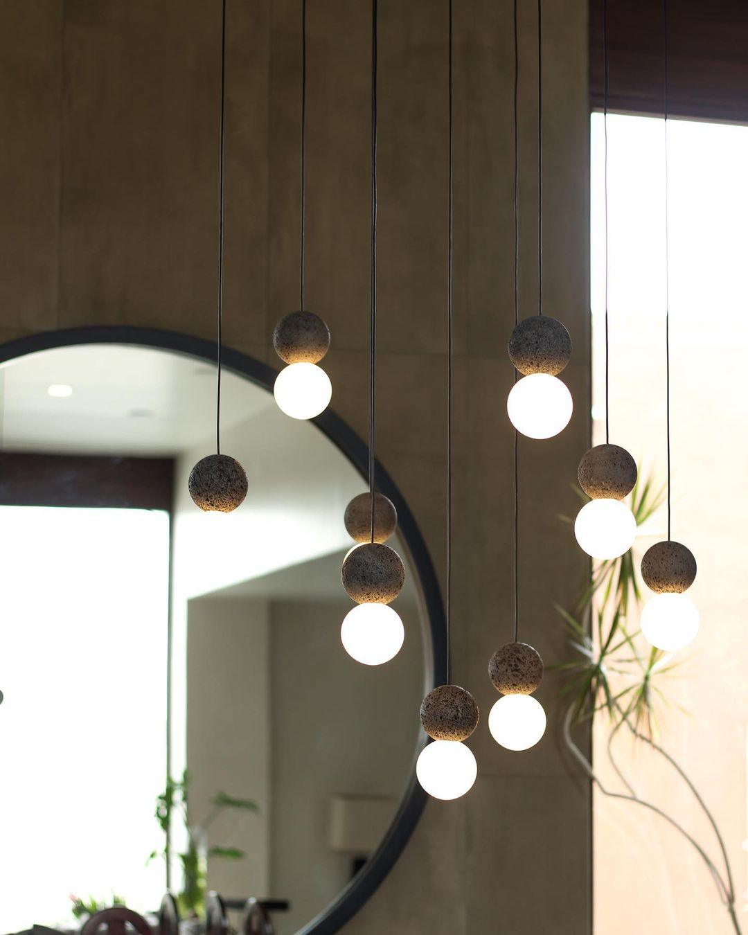 This Clérachic pendant cluster hangs beside a round black-framed mirror and a leafy plant against a warm wood wall.