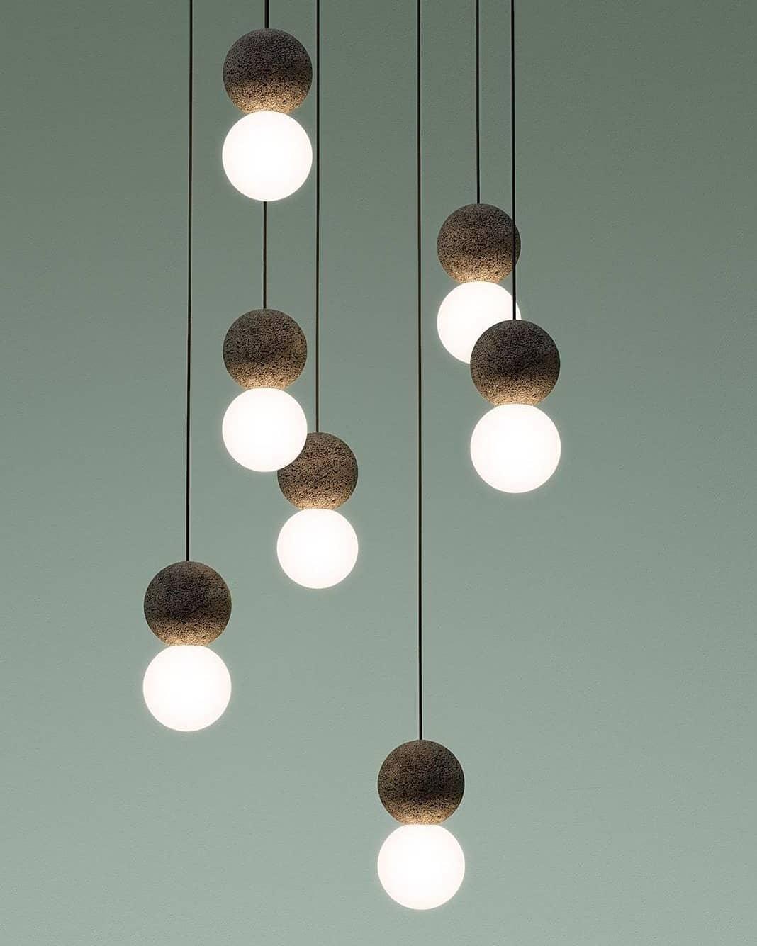 Several Clérachic pendants cluster together against a sage-green wall, their dark spheres and glass globes staggered at different heights.