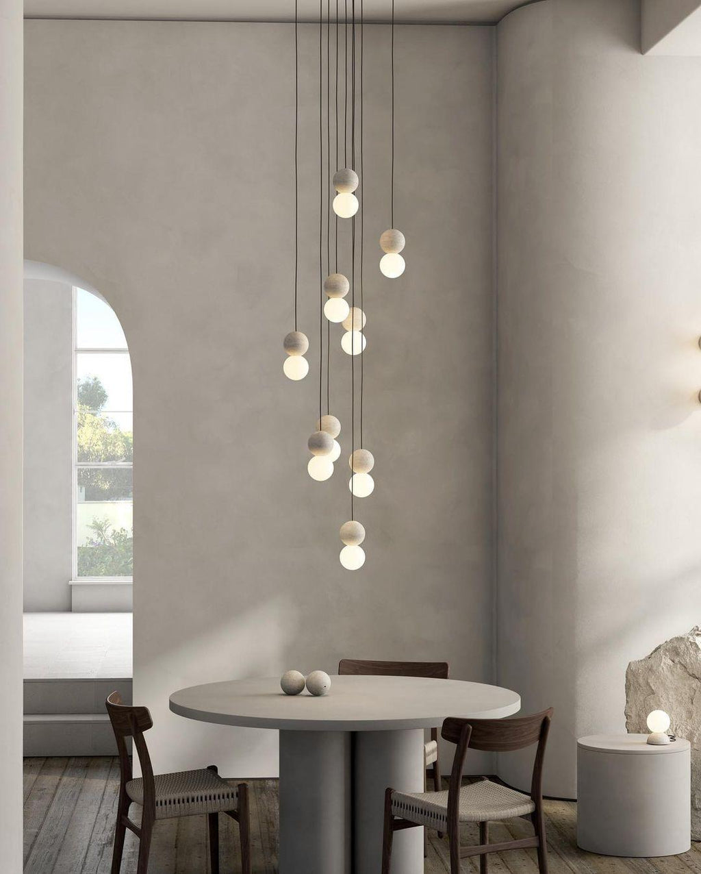 A cluster of pale sphere pendants from this Clérachic collection hangs above a round dining table near an arched window.