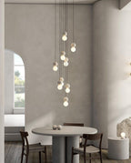 A cluster of pale sphere pendants from this Clérachic collection hangs above a round dining table near an arched window.