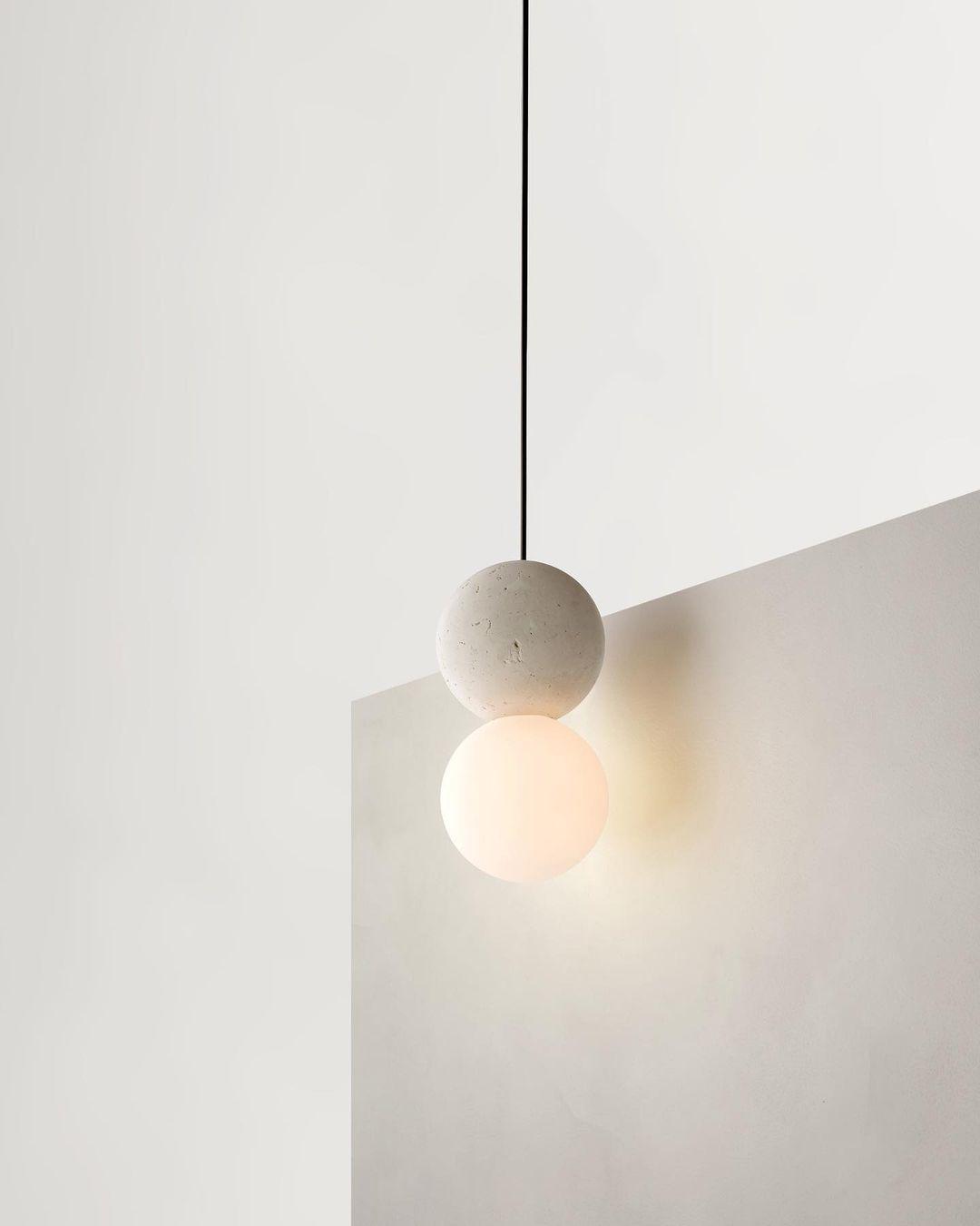 Close view of this Clérachic pendant, a stone-textured sphere set above a glass globe, against a two-tone painted wall.