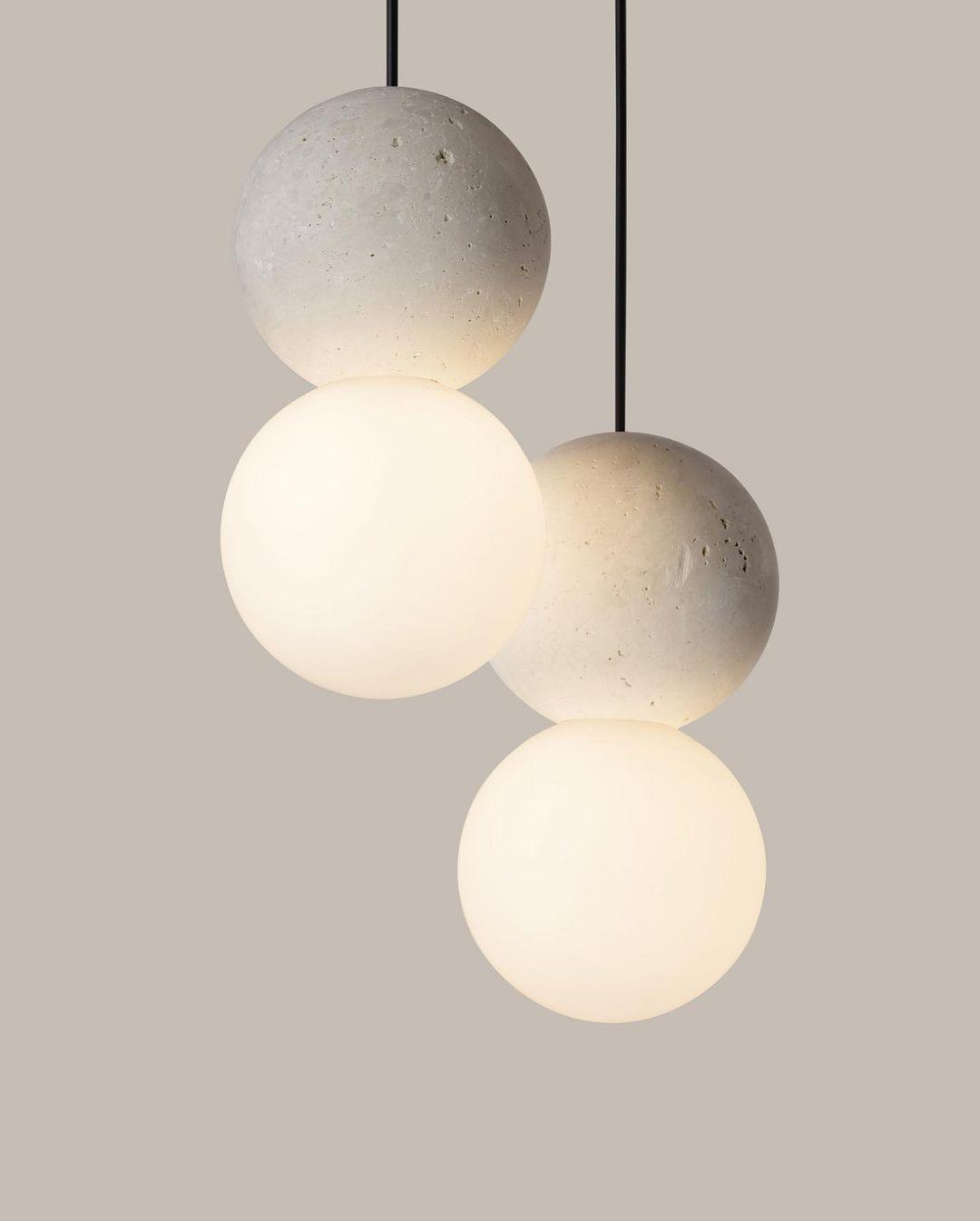Four Clérachic pendants cluster together, their grey stone spheres and opal glass globes set against a warm beige wall.