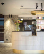 This Clérachic pendant hangs above a curved reception counter, its dark sphere and glass globe set against a rough stone wall.