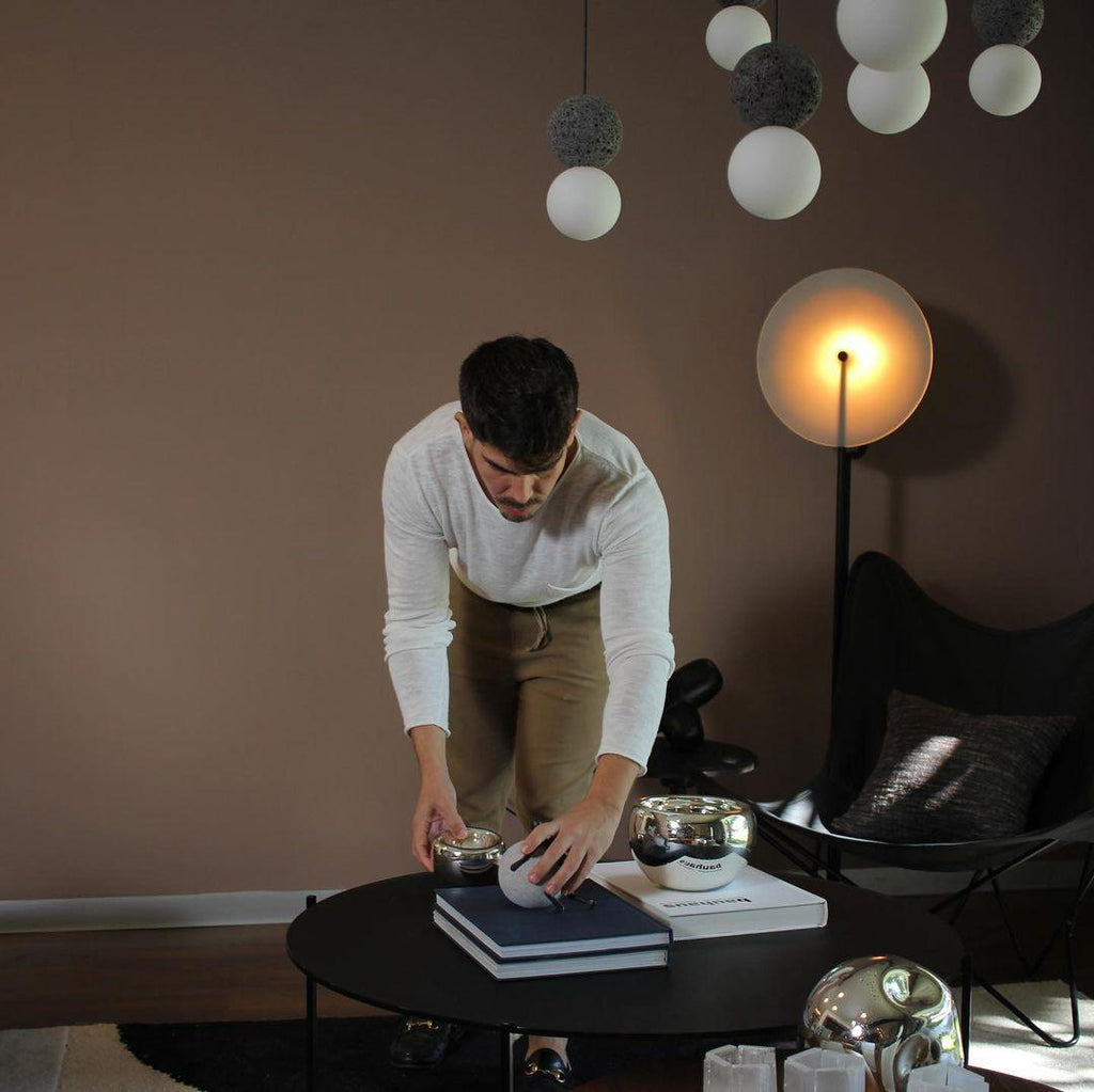 A cluster of pale sphere pendants from this Clérachic collection hangs above a low table, where a man arranges small objects.
