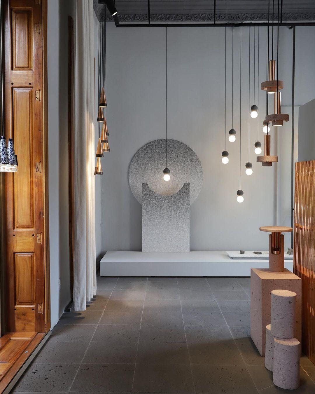 A showroom display mixes wood-cone and dark stone pendants, including this Clérachic pendant, near a round textured wall form.