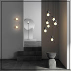 A vertical string of Clérachic pendants lights a staged room with stairs, a floor lamp and wall sconces nearby.