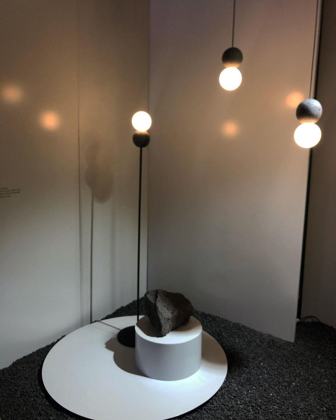 Clérachic pendants surround a round white side table holding a small rock, their light casting patterned shadows on the wall.