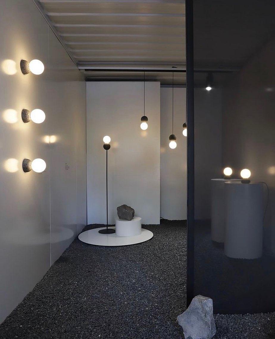 Several Clérachic pendants line a dim corridor, lighting a stone plinth and terrazzo floor between concrete walls.