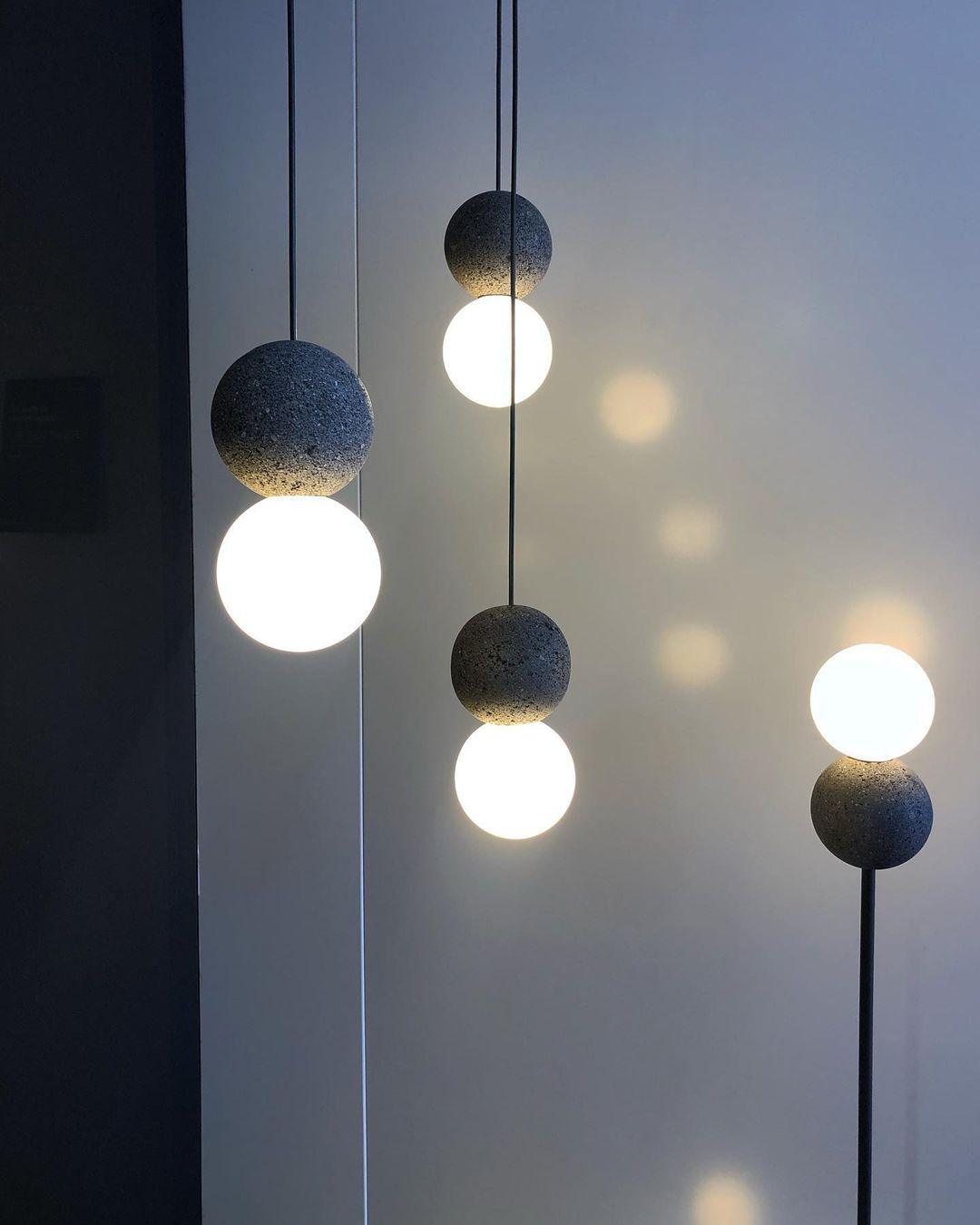 Several Clérachic pendants hang at staggered heights, their dark spheres and glass globes reflected on a pale blue wall.