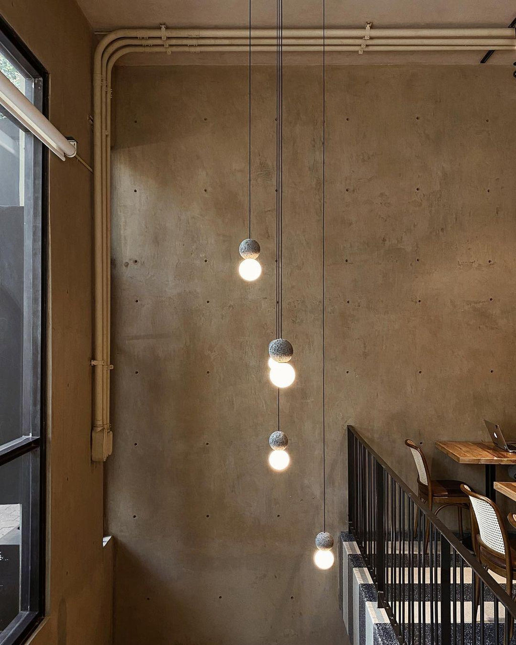 A string of Clérachic pendants lights a stairwell along a raw, weathered concrete wall.