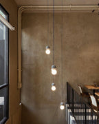 A string of Clérachic pendants lights a stairwell along a raw, weathered concrete wall.