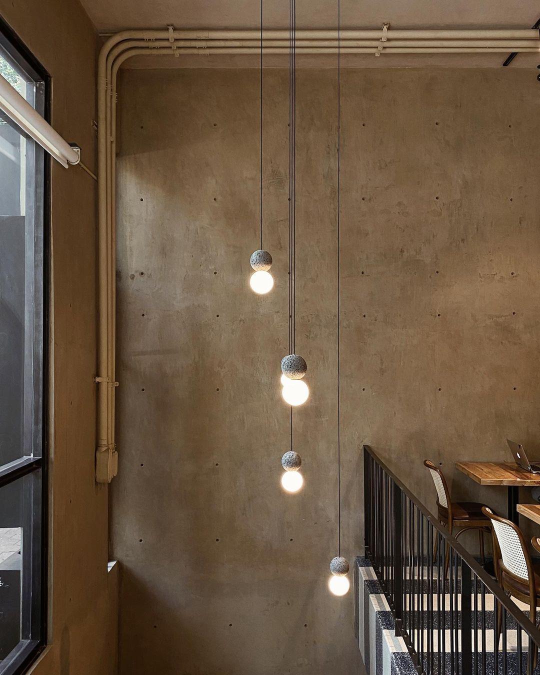 A string of Clérachic pendants lights a stairwell along a raw, weathered concrete wall.