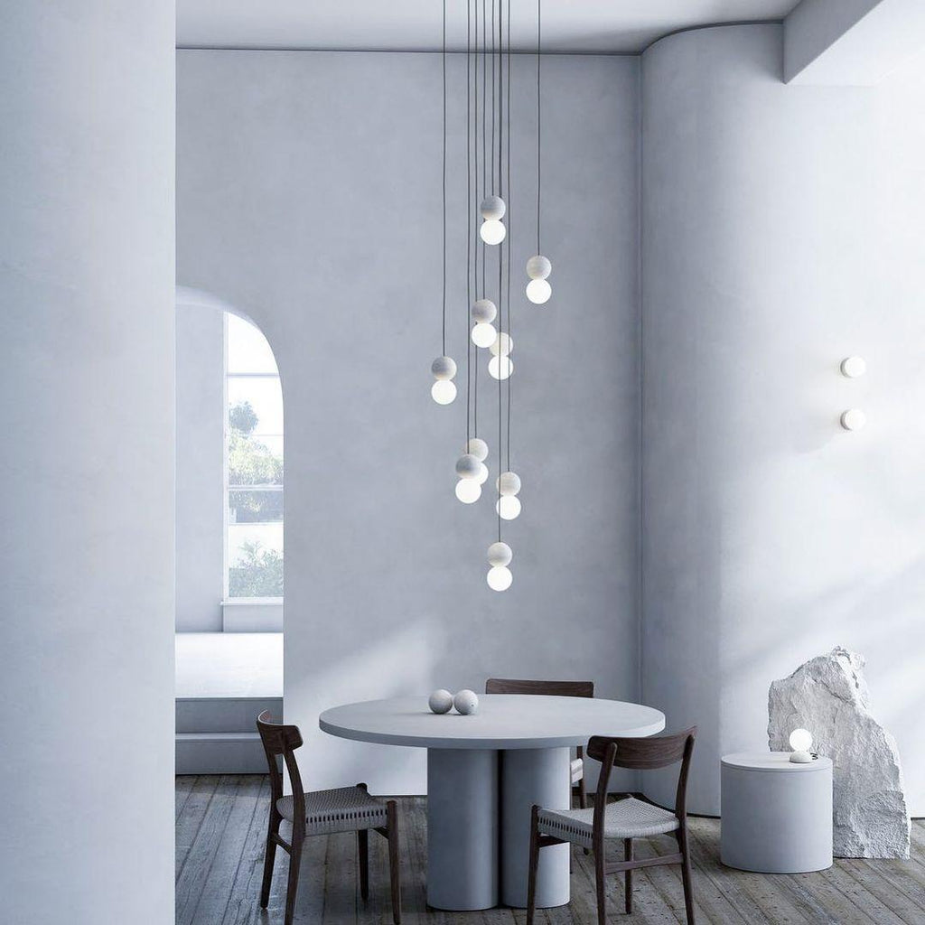 A tall cluster of Clérachic pendants drops above a round dining table in a curved, arch-windowed room.