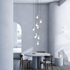 A tall cluster of Clérachic pendants drops above a round dining table in a curved, arch-windowed room.