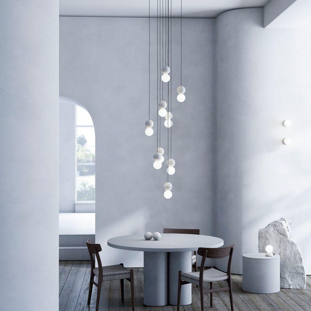A tall cluster of Clérachic pendants drops above a round dining table in a curved, arch-windowed room.