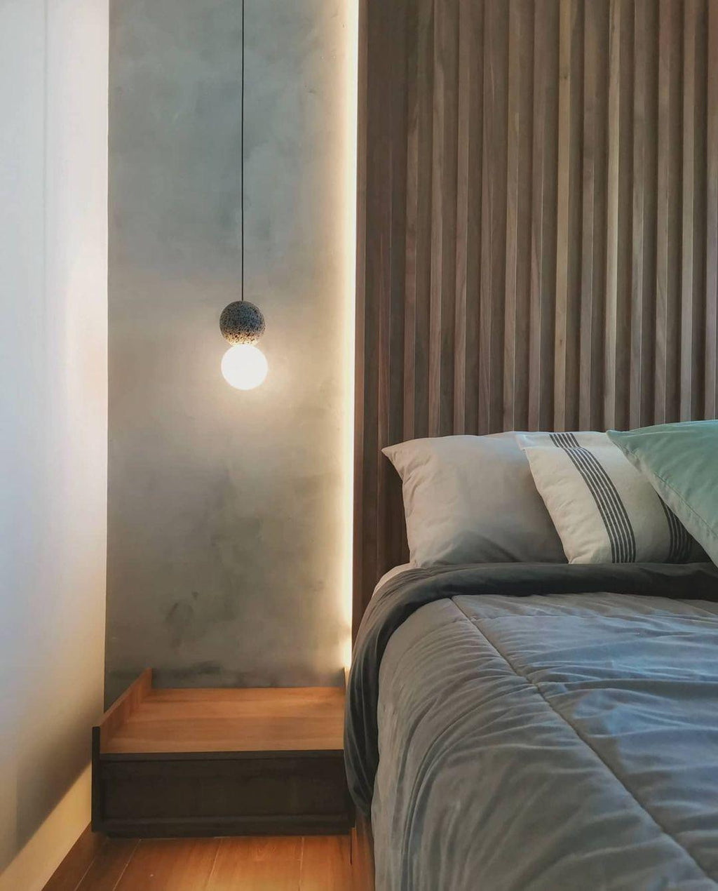 This Clérachic pendant hangs beside a bed with a wood-slat headboard, lit softly against a cove-lit wall.