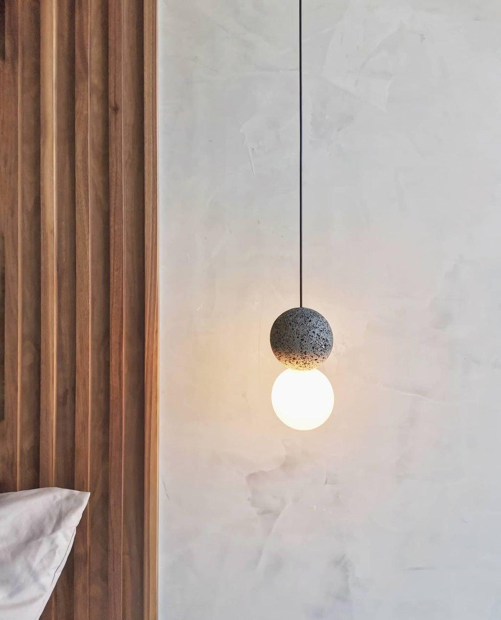 This Clérachic pendant hangs against a textured plaster wall, beside a strip of natural wood panelling.