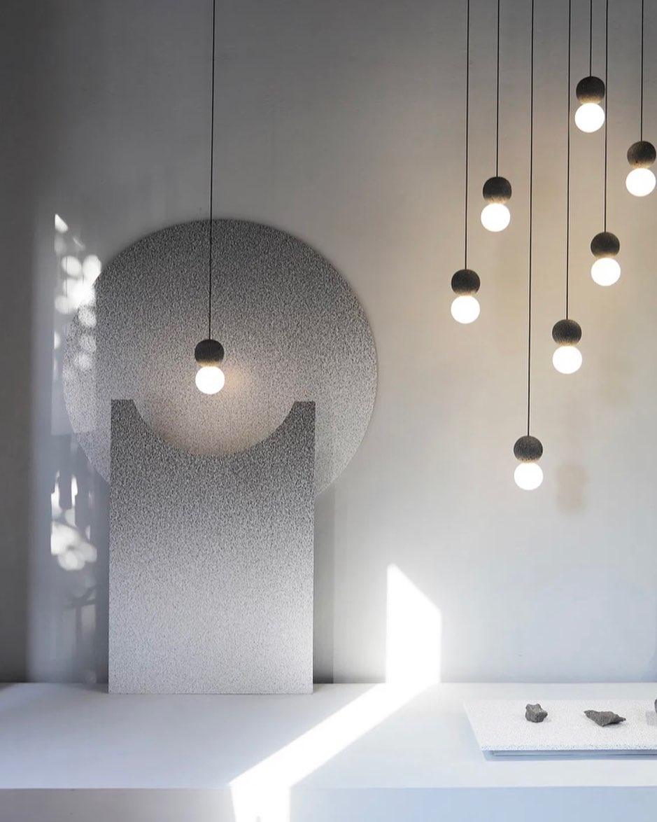 This Clérachic pendant, a single dark sphere and glass globe, hangs beside a tall arched wall form in a sunlit gallery.