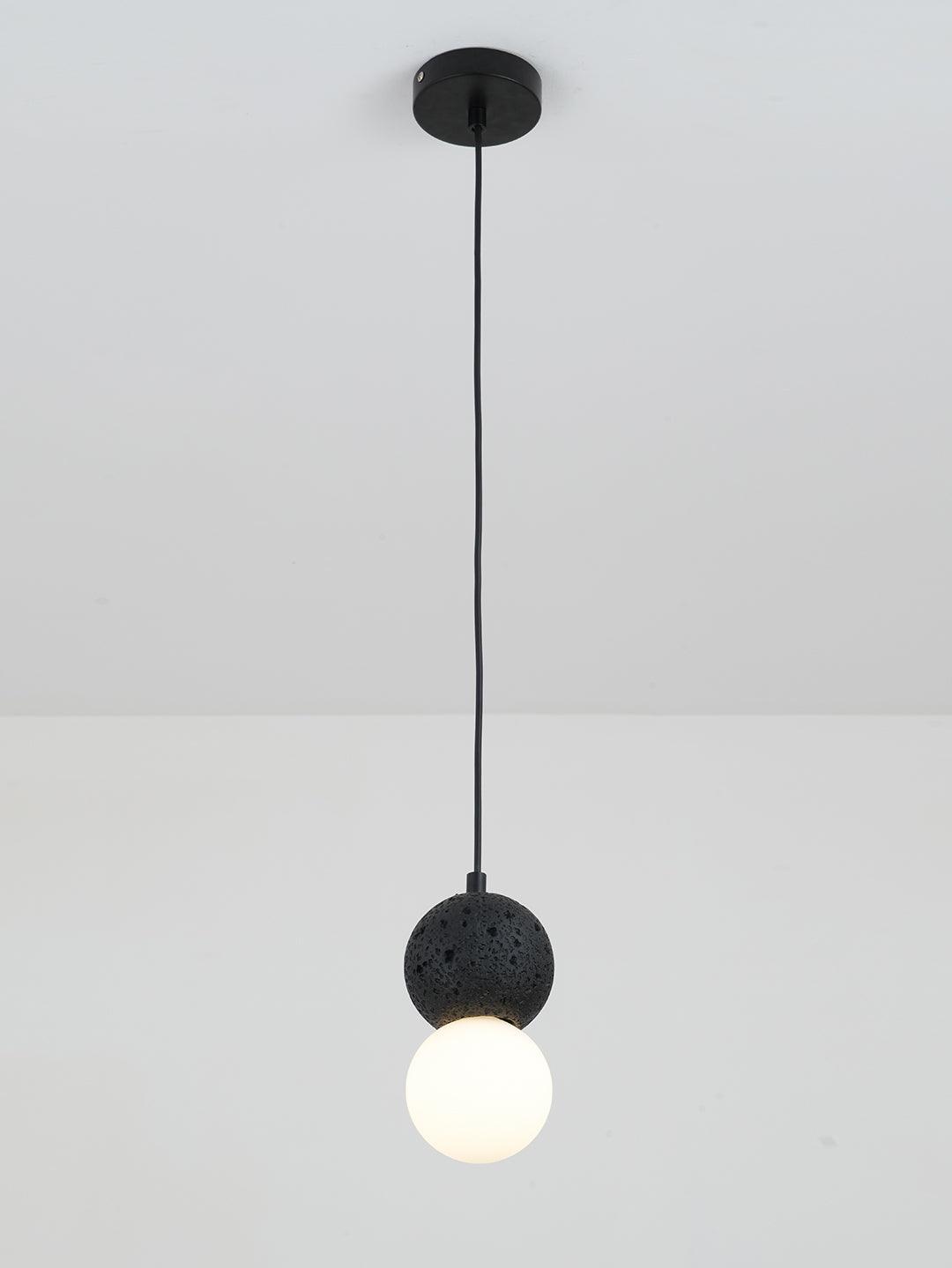 This Clérachic pendant, a dark textured sphere above an opal glass globe, drops from a plain white ceiling on a black cord.