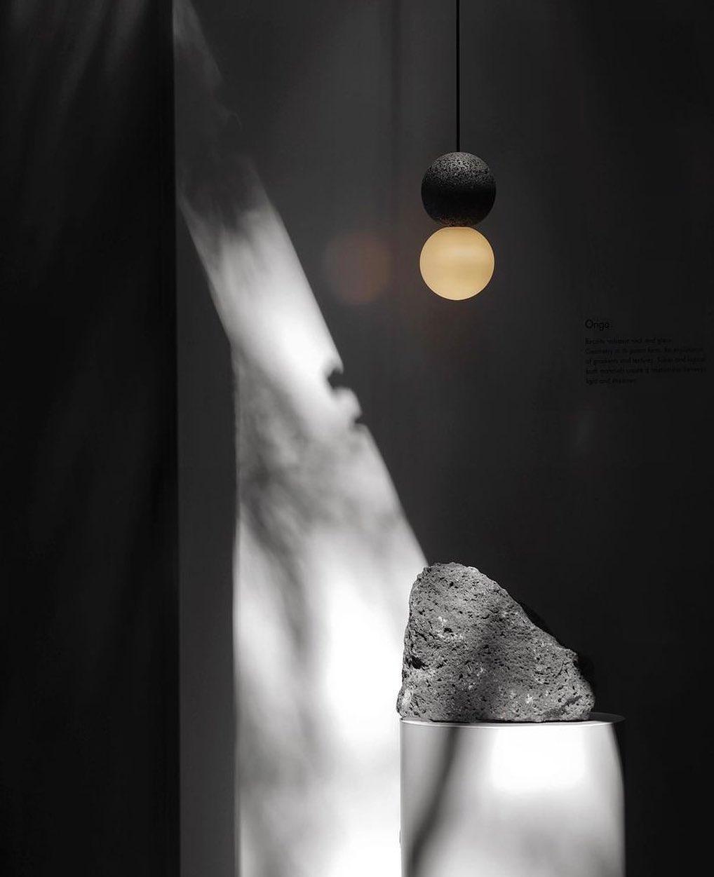 A single Clérachic pendant lights a rough stone fragment on a plinth, its glow cutting through a dark, shadowed room.