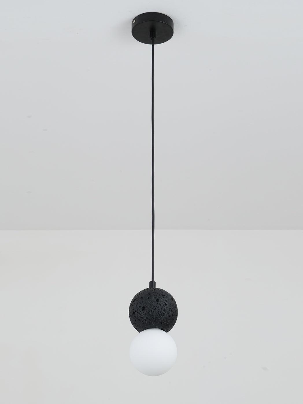 A single Clérachic pendant with a dark textured sphere and an opal glass globe drops from a plain white ceiling.