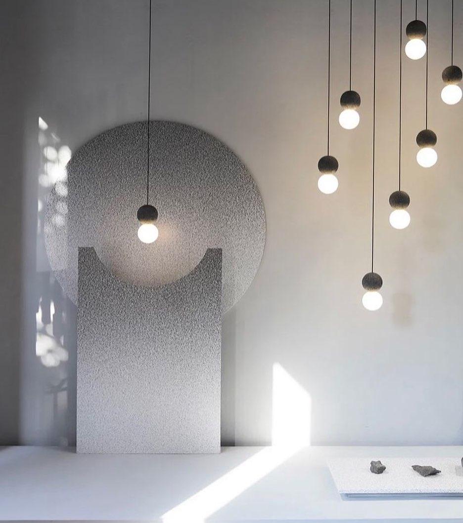 Clérachic pendants of varying lengths hang beside a rounded concrete wall form in a sunlit gallery space.