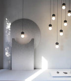 Clérachic pendants of varying lengths hang beside a rounded concrete wall form in a sunlit gallery space.
