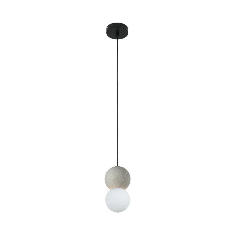 A grey stone-textured sphere tops this Clérachic pendant, its opal glass globe set below on a black cord against white.