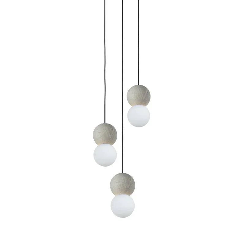 A three-light cluster of Clérachic pendants hangs together, grey stone spheres paired with opal glass globes at different lengths.