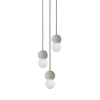 A three-light cluster of Clérachic pendants hangs together, grey stone spheres paired with opal glass globes at different lengths.