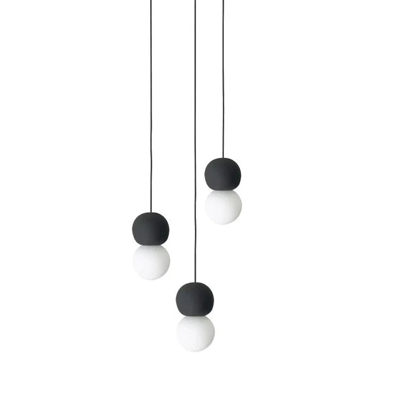 A three-light cluster of Clérachic pendants hangs together, dark stone spheres paired with opal glass globes at staggered heights.