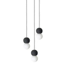 A three-light cluster of Clérachic pendants hangs together, dark stone spheres paired with opal glass globes at staggered heights.