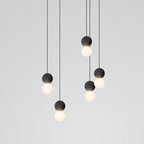 This Clérachic pendant cluster fans out in a loose spiral, dark stone spheres and glass globes glowing against plain grey.