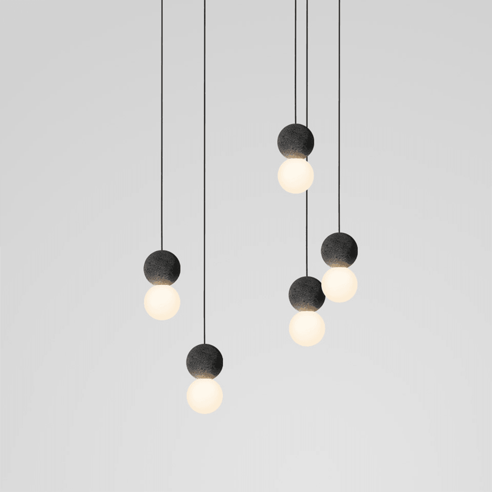 This Clérachic pendant cluster fans out in a loose spiral, dark stone spheres and glass globes glowing against plain grey.