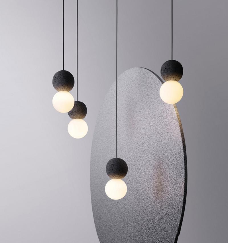 A cluster of dark stone pendants with opal glass globes from this Clérachic collection hangs beside a large grey sculptural panel.