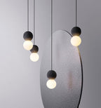 A cluster of dark stone pendants with opal glass globes from this Clérachic collection hangs beside a large grey sculptural panel.