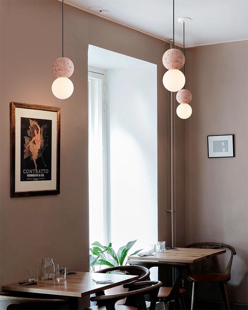 Clérachic pendants, including a dusty-pink sphere, hang beside a window in a warm-toned dining room with framed art.