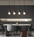 Four dark stone pendants with opal glass globes from this Clérachic collection hang in a row above a grey dining table and chairs.
