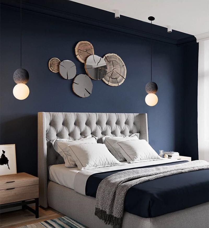 This Clérachic pendant hangs in a navy-painted bedroom, near a cluster of wood slice wall decor above a tufted headboard.