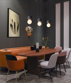 Three Clérachic pendants hang above a dining table with a burnt-orange banquette and dusty-pink chairs.